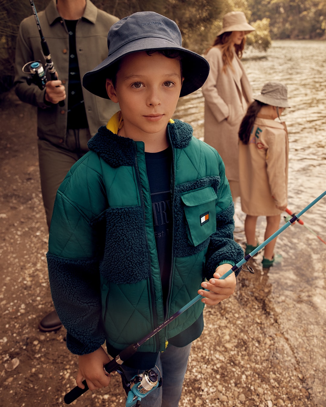 A boy fishing by a stream, wearing Tommy Hilfiger
